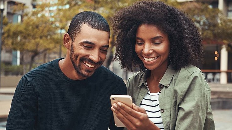 A man and a woman laughing and looking at a smartphone